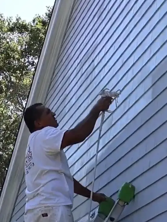 Painter spraying the exterior siding of a house